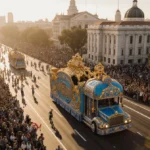 Rose Parade float Belonging glides past Pasadena landmarks with blue and gold design glowing in golden light