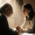 Salman Rushdie and Rachel Eliza Griffiths sit together with clasped hands under warm golden light and books nearby.