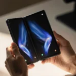 Hands hold open Samsung Galaxy Z Fold 7 with sleek foldable screen showing on minimalist desk with soft warm light