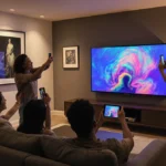 Friends admire art on Samsung Frame TV above sofa with tablet and wall prints nearby