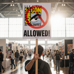 ComicCon attendee holding a No AI Art Allowed sign with a busy exhibit hall and warm natural light