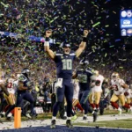 Seahawks quarterback Geno Smith celebrating touchdown with arms raised as teammates rush over with confetti falling and score