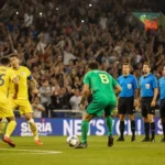 Green-clad player stands dejected with yellow team celebrating goal save and refs nearby
