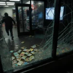 Blurred figure fleeing from shattered storefront window with Pokémon sports cards and security footage