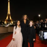 Shonda Rhimes walking red carpet with daughters and Eiffel Tower behind them