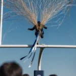 Skydiver caught in netting with threads and parachute ribbon trailing toward ground above goal post.