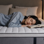 Person sleeping peacefully on waterproof mattress protector with soft warm lighting and a glass of water nearby.