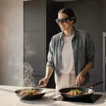 Tech reviewer wearing smart audio glasses while cooking with sizzling pan and smartphone resting on modern kitchen counter