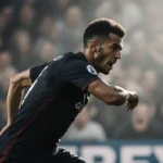 Soccer player sprinting with raised elbow and intense expression near blurred stadium crowd