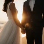 Sonia Mena and Spencer House hold hands on the beach with sunset glow and palm trees behind them