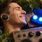Person wearing Soundcore P20i earbuds while relaxing among vintage audio equipment with blue light glowing from earbuds