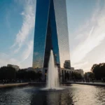 State Street glass tower reflects in water with sunrise sky and pedestrians admiring the financial district landmark