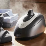 Steam cleaner resting on wooden surface with neatly folded clothes and natural light highlighting the gleaming metal