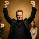 Stellan Skarsgård raises arms in triumph with elegant wife and golden florals celebrating success