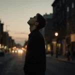 Stephen Graham walking alone down dim street with warm city lights and contemplative expression