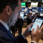 Anxious investor checking phone with stock market crash headline while traders rush past in dim trading floor