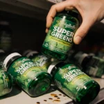 Person recoils from contaminated greens supplement bottle with scattered bottles on store shelf