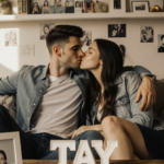 Taylor Lautner kisses his wife on the cheek while she leans into him on a cozy couch with a coffee table book titled Tay.