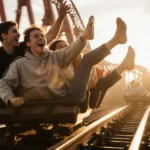 Teenagers surfing roller coaster train with feet dangling and motion blur while laughing with friends watching