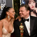 Teyana Taylor and Leonardo DiCaprio laughing together with Golden Globes trophy between them and K-pop posters behind