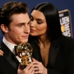 Timothée Chalamet holds his Golden Globe award while Kylie Jenner touches his cheek with warm golden lighting