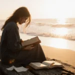 Tish Cyrus sits alone on wooden beach at sunrise with leather book in hands and journal pages scattered beside her