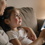 Three-year-old girl looking up at mother with tears while mother gently places hand on shoulder on couch phone pregnancy