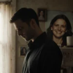 Travis Clark stands alone with head bowed near faded family photos and Katie Bates