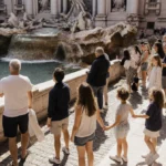 Tourists standing on Trevi Fountain steps looking up with warm sunlight and baroque fountain in background