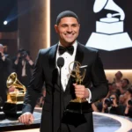 Trevor Noah holding Grammy Award with stage lights and trophies behind him