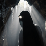 Cave explorer walking with headlamp glow illuminating misty walls and dripping water in darkness.