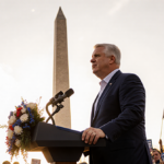 Vice President JD Vance speaking at podium with flag in hand during March for Life rally and Washington Monument behind