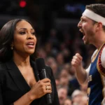 Vanessa Williams singing national anthem with heckler standing and shouting while shocked audience watches