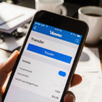 Smartphone screen shows Venmo transfer toggle in bright blue with blurred office and coffee.