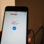 Smartphone screen shows restored Verizon home screen with blue checkmark and cityscape view through window