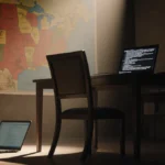 Abandoned chair pushed back from war room table with open laptop showing error messages and US map on wall