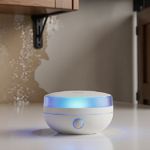 Smart home water sensor glows with blue LED on white countertop and faint water damage on cabinet wall