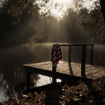 Weathered wooden dock stretches into still pond with child