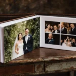 Happy bride and groom pose beside wedding album with shocked guests behind them showing unexpected photos