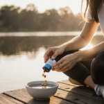 Woman pouring wellness supplement into bowl with calm dawn lake and warm light