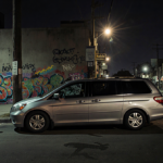 Silver Honda Odyssey sits at an angle with nighttime shadows and street art in a gritty urban setting