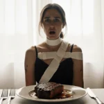 Woman sits at dinner table with half-eaten steak and medical bandages showing choking incident