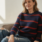 Woman sitting on plush couch with navy blue and red stripe sweater and natural light highlighting her cozy effortless style