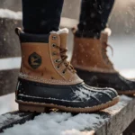 Worn waterproof duck boot rests on snowy bench with scratches and warm light