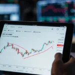 Trader gripping tablet showing XRP chart with red $2.00 pivot line and dim trading floor behind